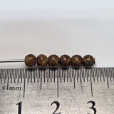 Brown beads on a stick with a ruler for scale on a white background