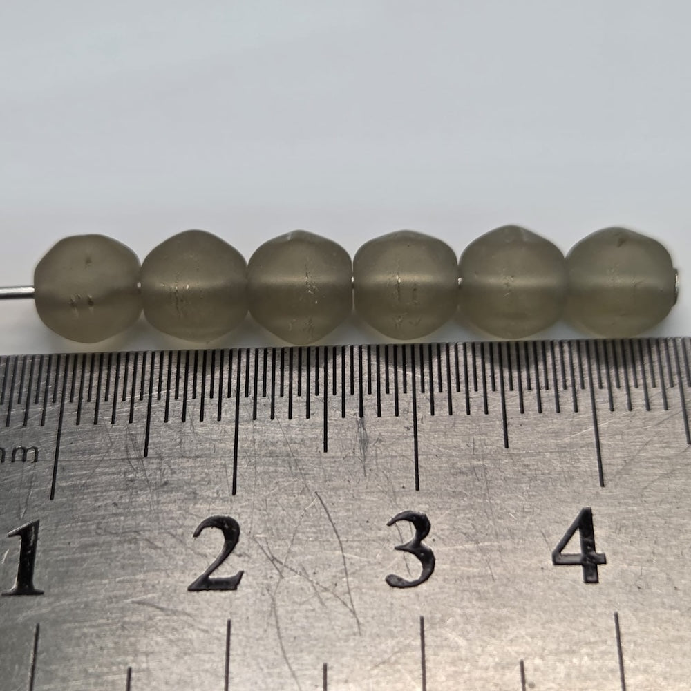 Close-up of translucent grey frosted beads on a white background with a ruler for scale