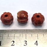 Three brown decorative beads with a ruler at the bottom for size reference on a white background.