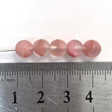 Pink beads on a metal ruler for size reference