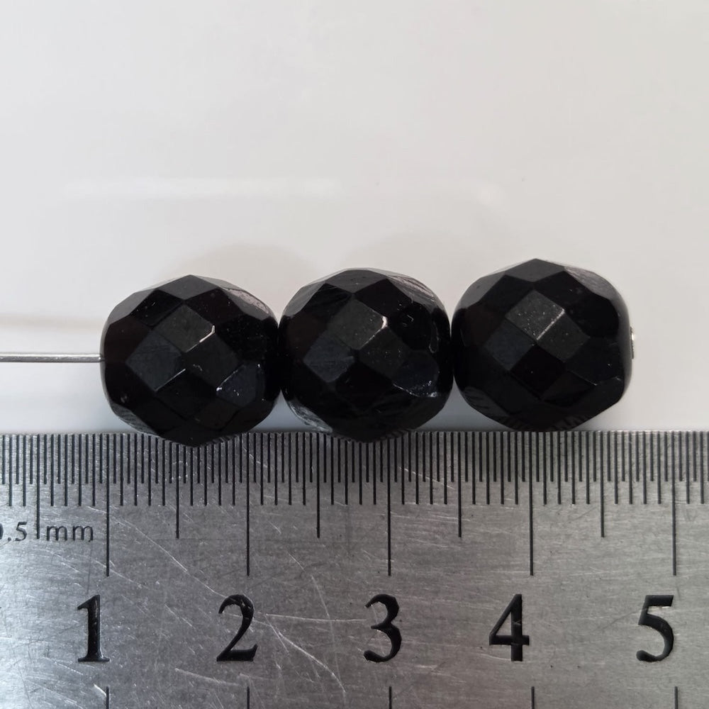 Three black faceted beads next to a ruler on a white background