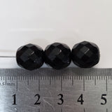 Three black faceted beads on a ruler for size reference