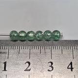 Green beads on a metal rod with a ruler for scale on a gray background