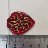 Red glass pendant Hajj with gold inscription next to a ruler for scale
