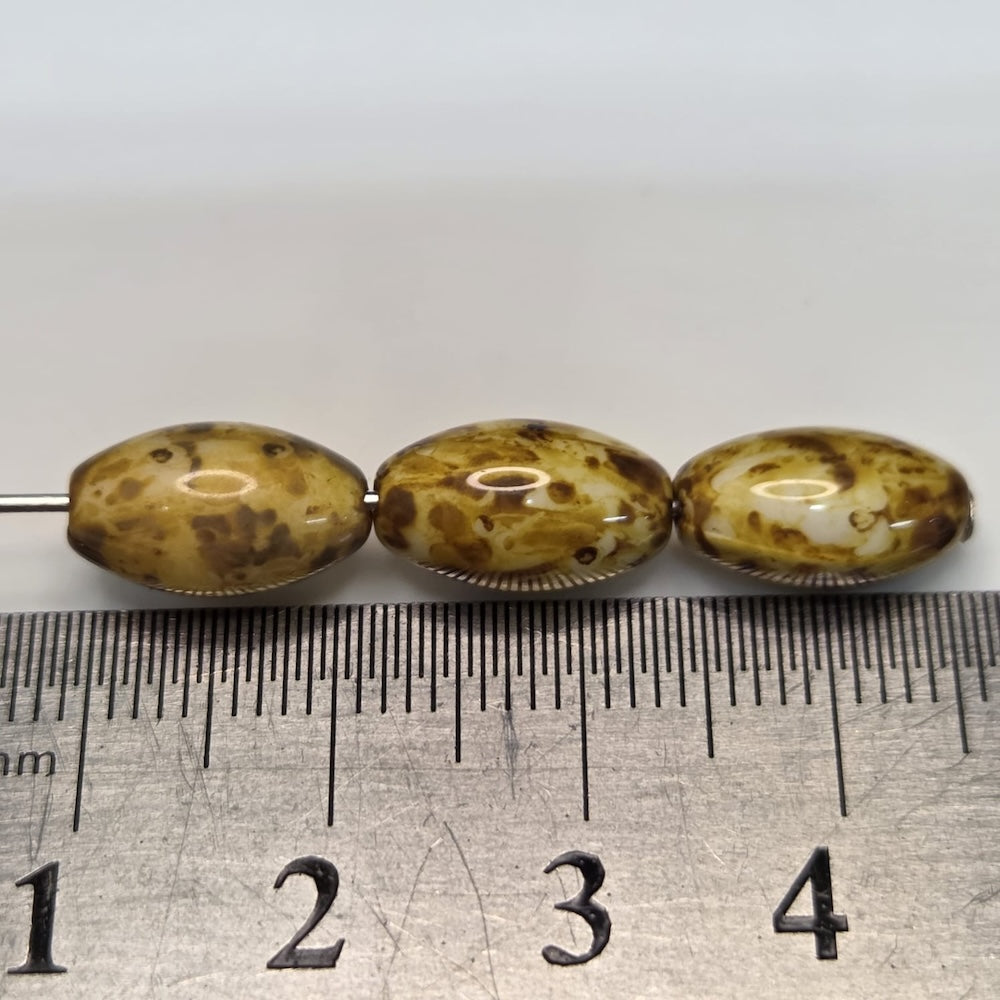 Three speckled brown beads on a ruler for size reference