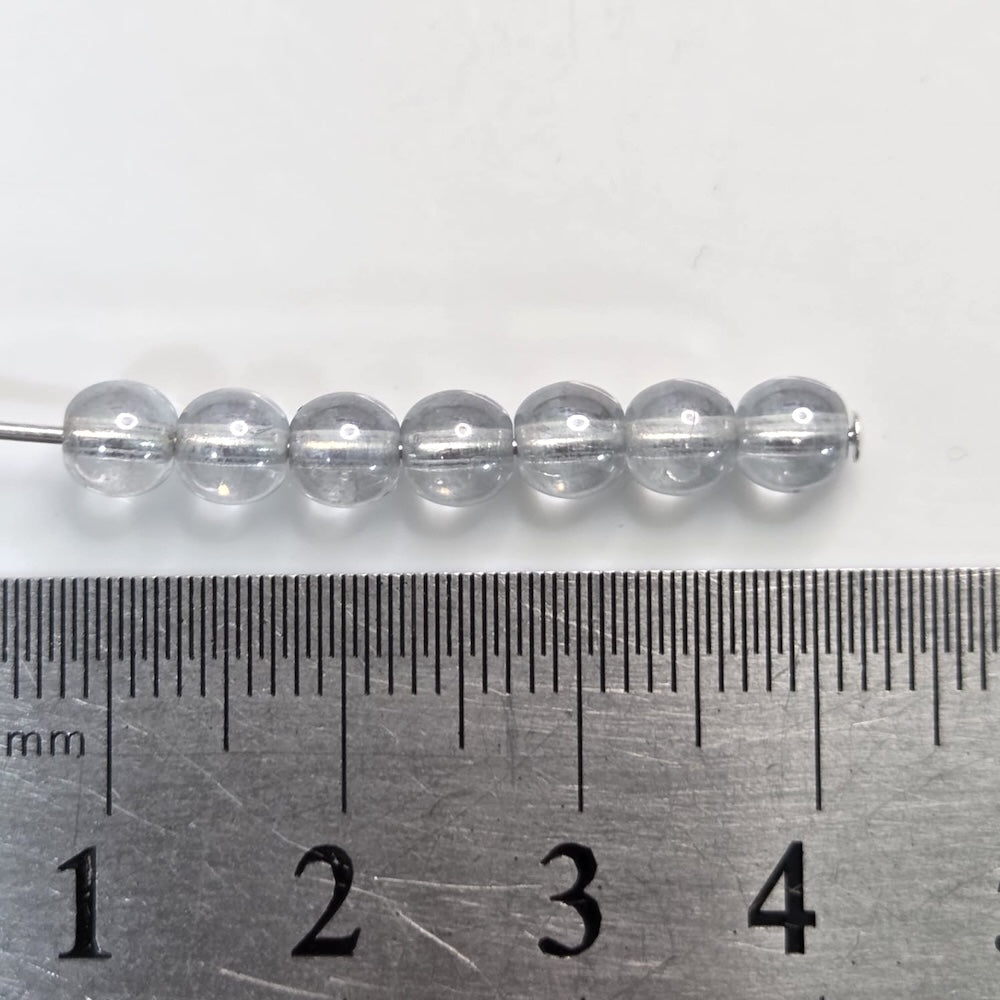 light blue beads on a metal ruler for size reference