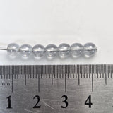 light blue beads on a metal ruler for size reference