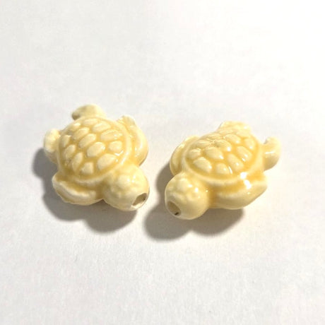 Two yellow turtle-shaped porcelain ceramic beads on a white background