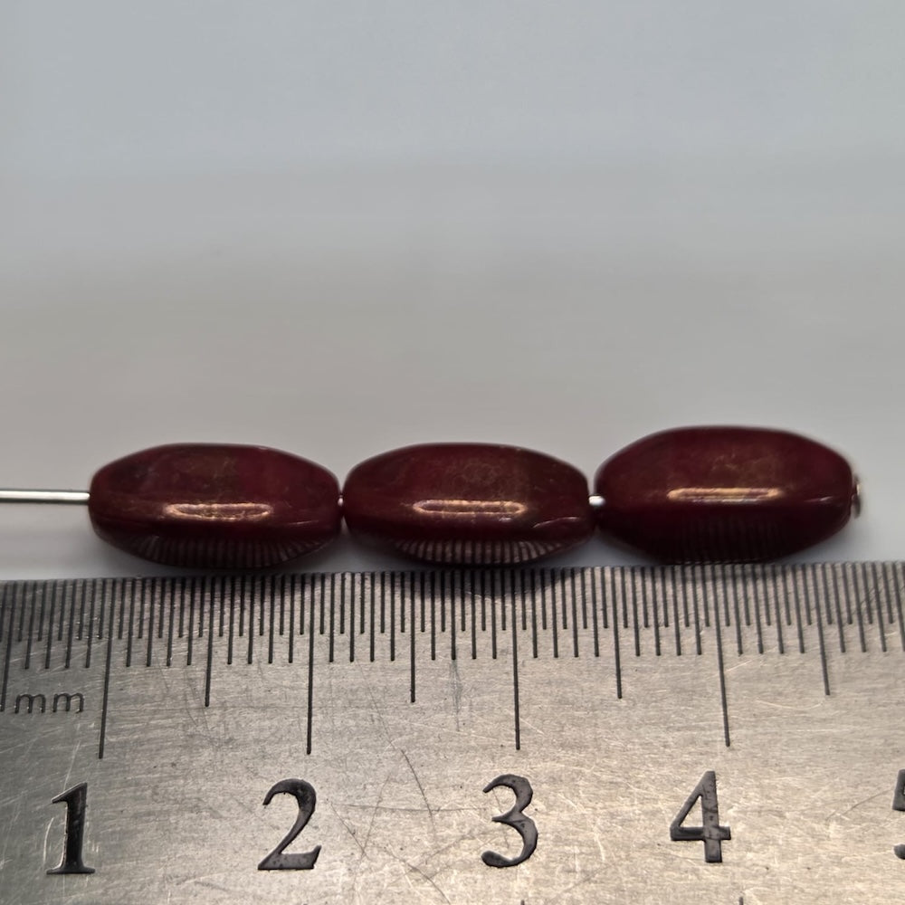 Three maroon beads on a metal rod with a ruler for scale against a gray background