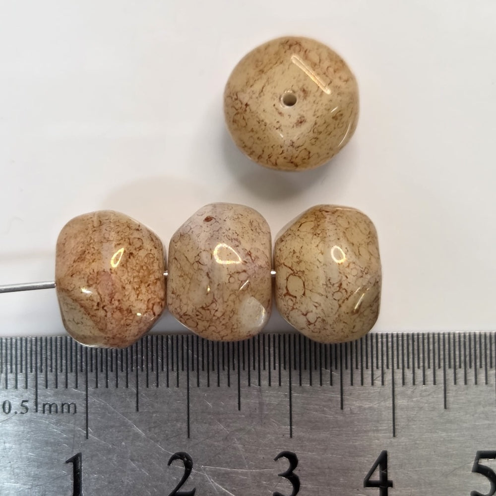 Four beige beads on a white background with a ruler for scale.