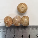 Four beige beads on a white background with a ruler for scale.