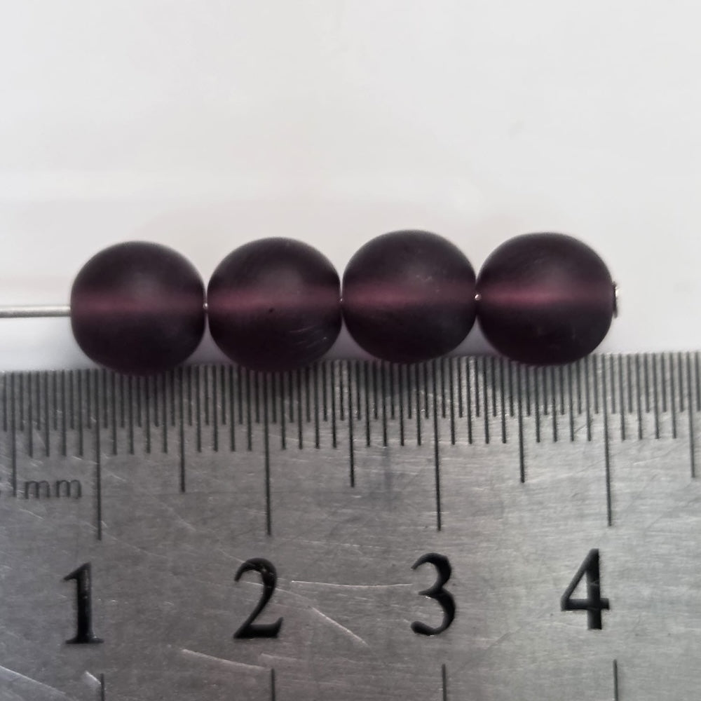 Four dark purple beads on a ruler for size reference