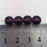 Four dark purple beads on a ruler for size reference