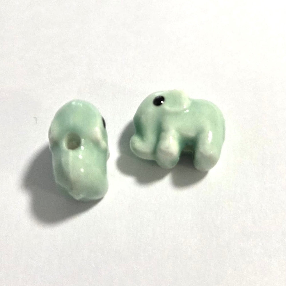 two light green elephant beads made from porcelain ceramic on a white surface