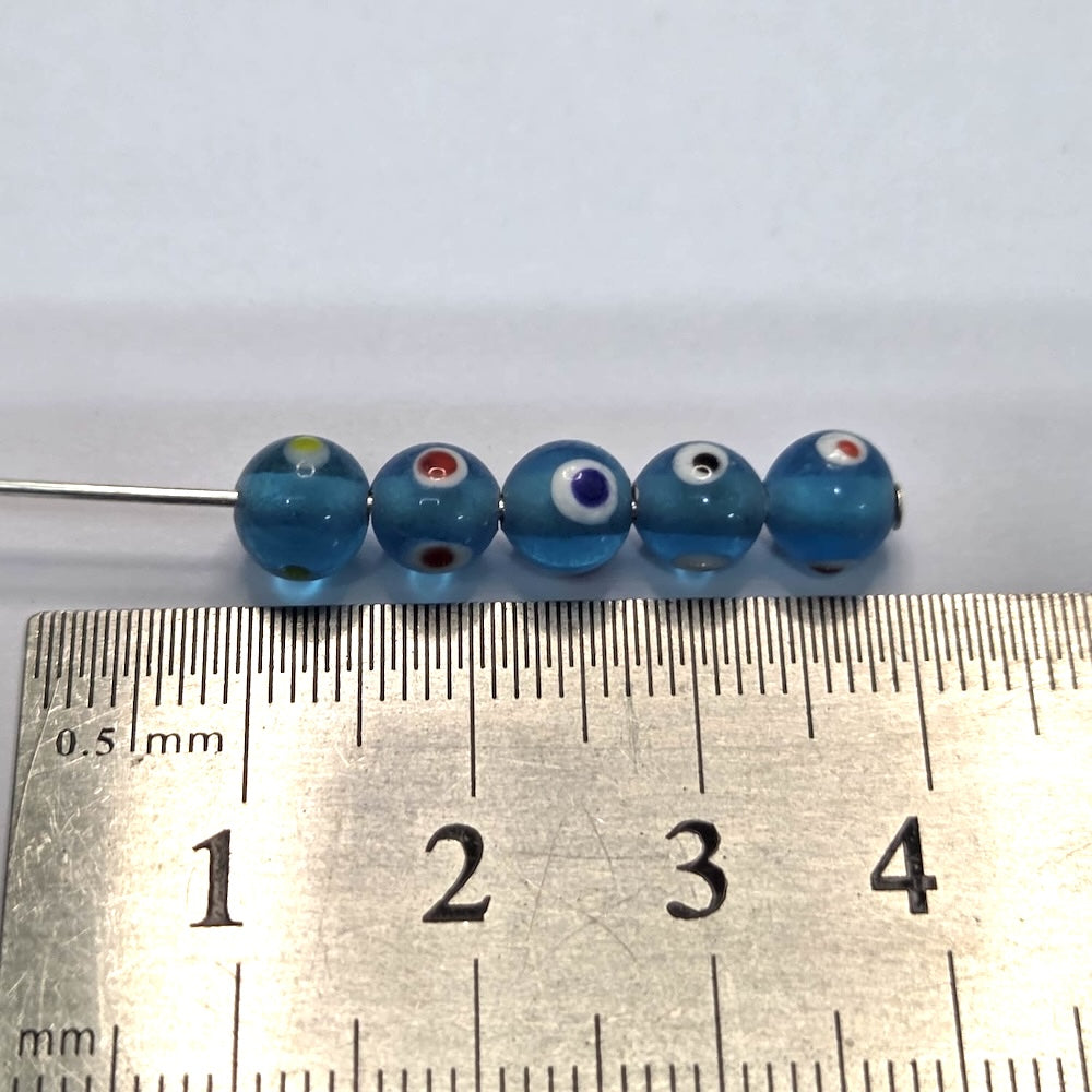 close up of aqua blue transparent beads with colourful eyes and showing threading holes for the purpose of making jewelry and craft with a ruler to show scale