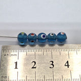 close up of aqua blue transparent beads with colourful eyes and showing threading holes for the purpose of making jewelry and craft with a ruler to show scale