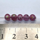 A collection of transparent pink glass beads with red yellow and white eyes, used for making jewelry with a ruler to show scale