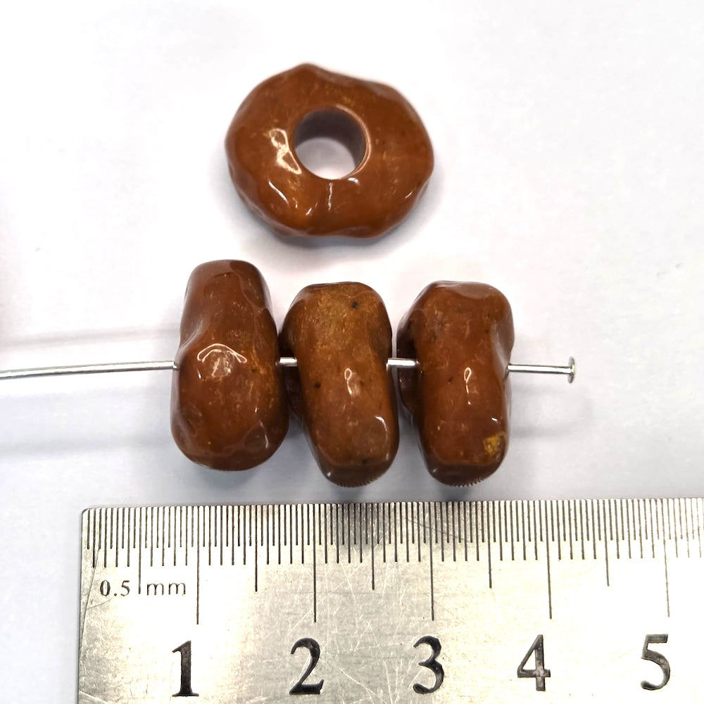 Three brown beads on a metal rod with a ruler for scale on a white background
