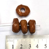 Three brown beads on a metal rod with a ruler for scale on a white background