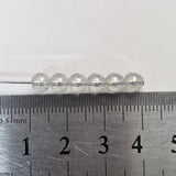 Clear beads on a pin with a ruler for scale on a white background