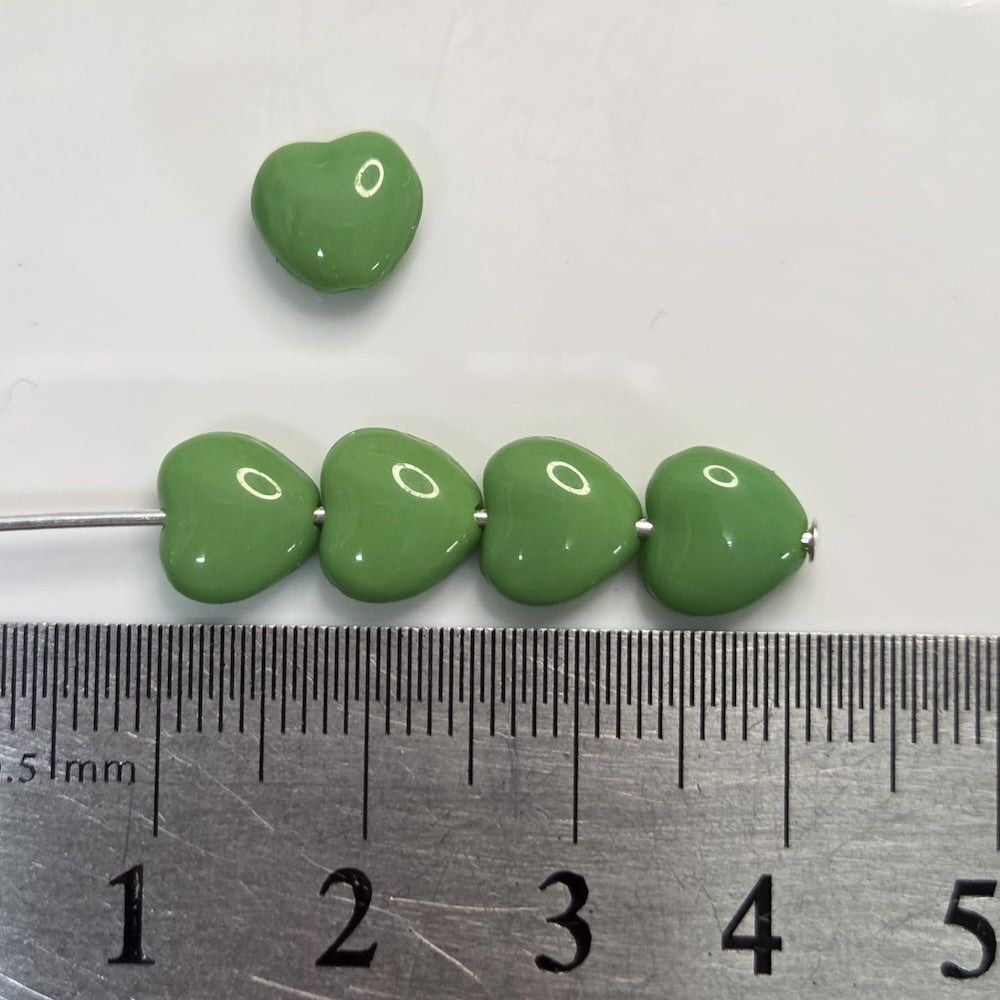 Green beads on a metal rod with a ruler for scale on a white background