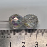 Close-up of clear faceted firepolish beads with iridescent colors on a white background with a ruler to show scale