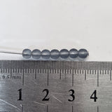 blue Gray beads on a needle with a ruler for scale on a white background