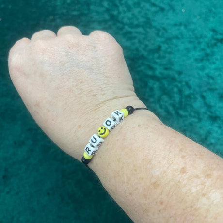 r u ok bracelet displayed on an arm on a green background