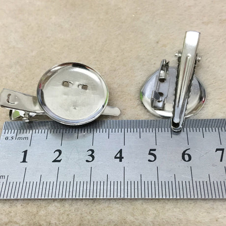 Two alligator style brooch settings on a textured fabric background with a ruler for scale.