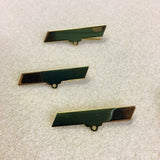 Three green and gold rectangular metal brooch fittings on a textured surface