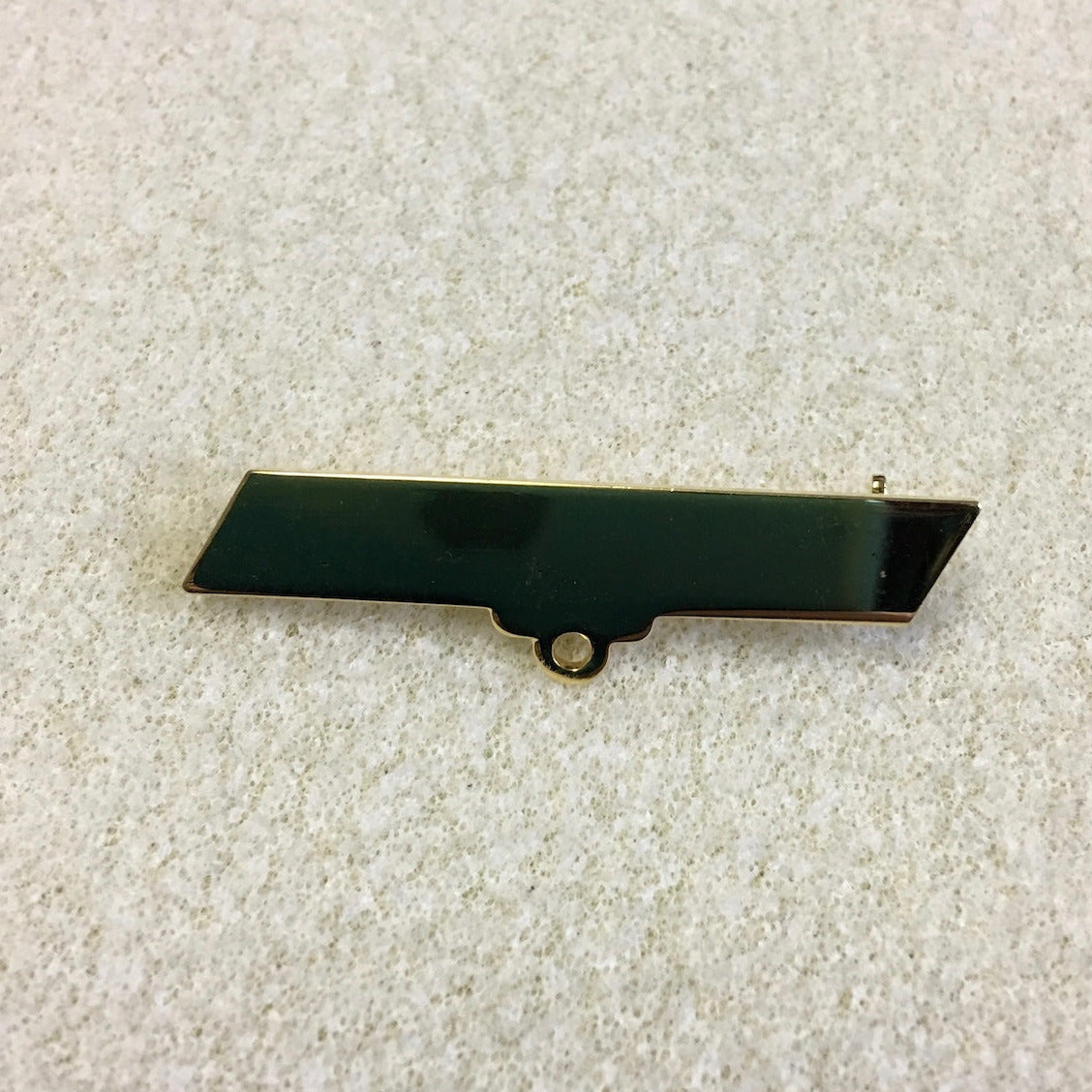 gold brooch bar fitting on a textured background showing a loop for attaching a pendant
