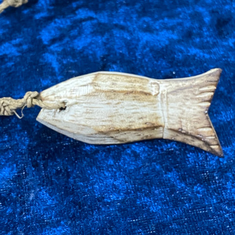 A hand-carved wooden fish-shaped decoration with a natural beige and brown color, displayed on a blue textured background.