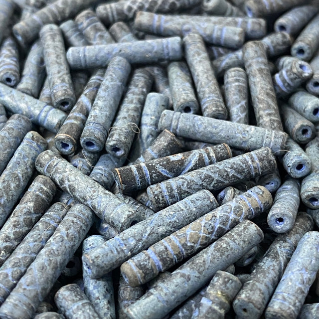 Close-up of a pile of blue cylindrical vintage ceramic beads with intricate patterns.