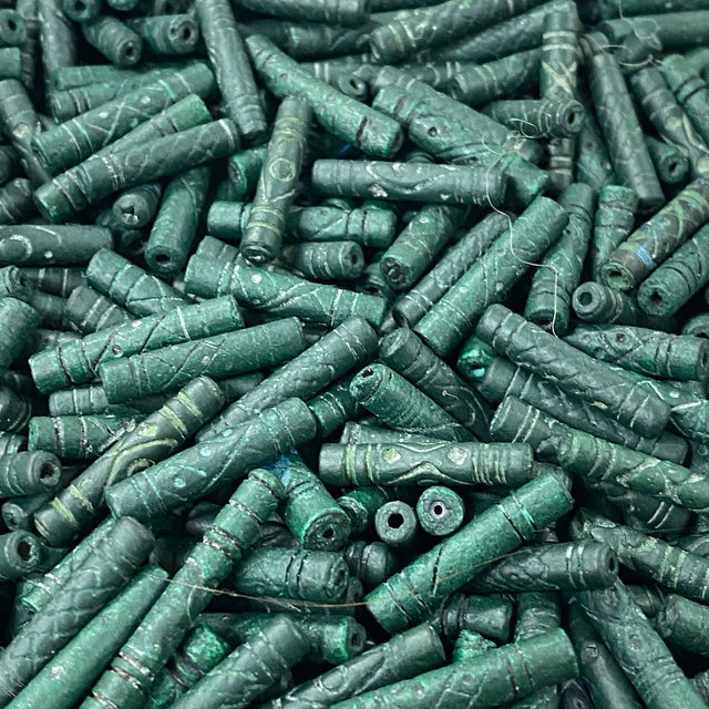 Close-up of a pile of green cylindrical vintage ceramic beads with intricate patterns.