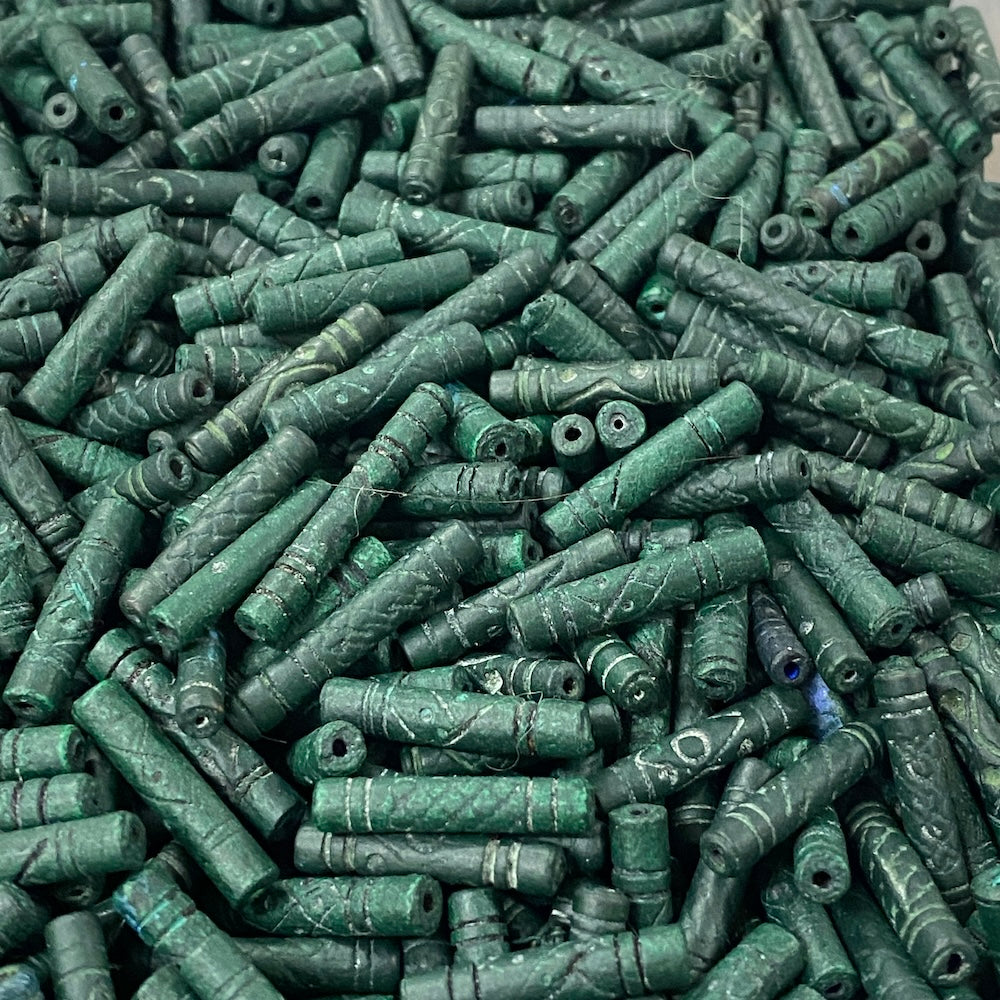 Close-up of a pile of green cylindrical vintage ceramic beads with intricate patterns.