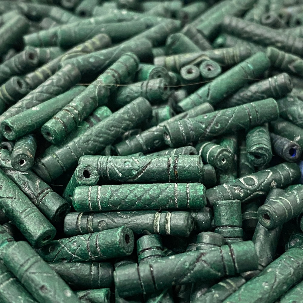 Close-up of a pile of green cylindrical vintage ceramic beads with intricate patterns.