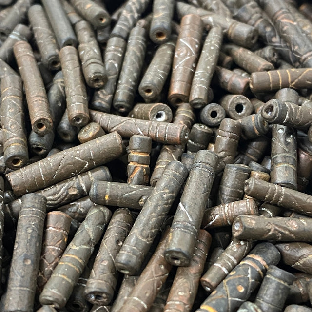 Close-up of a pile of dark brown cylindrical vintage ceramic beads with intricate patterns.