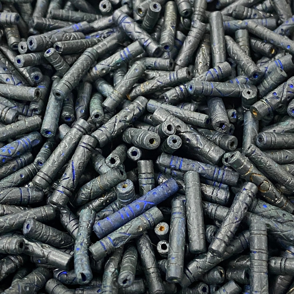 Close-up of a pile of dark blue cylindrical vintage ceramic beads with intricate patterns.