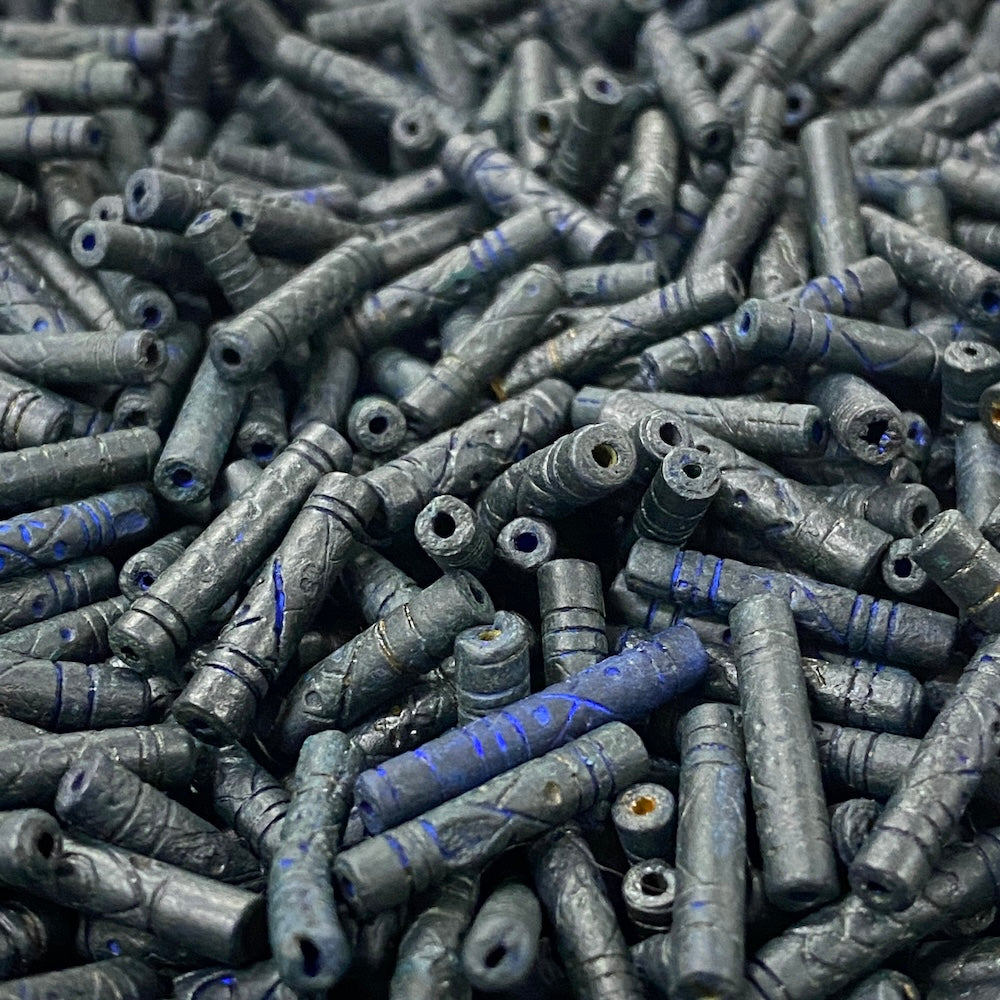 Close-up of a pile of dark blue cylindrical vintage ceramic beads with intricate patterns.