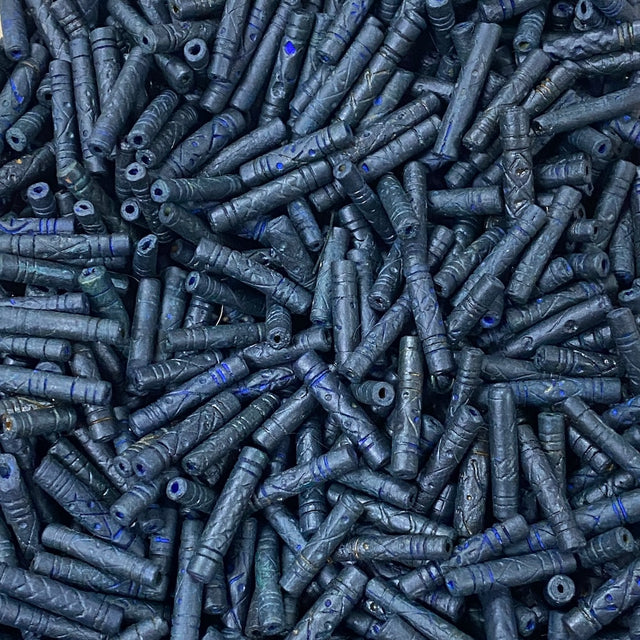 Close-up of a pile of dark blue cylindrical vintage ceramic beads with intricate patterns.