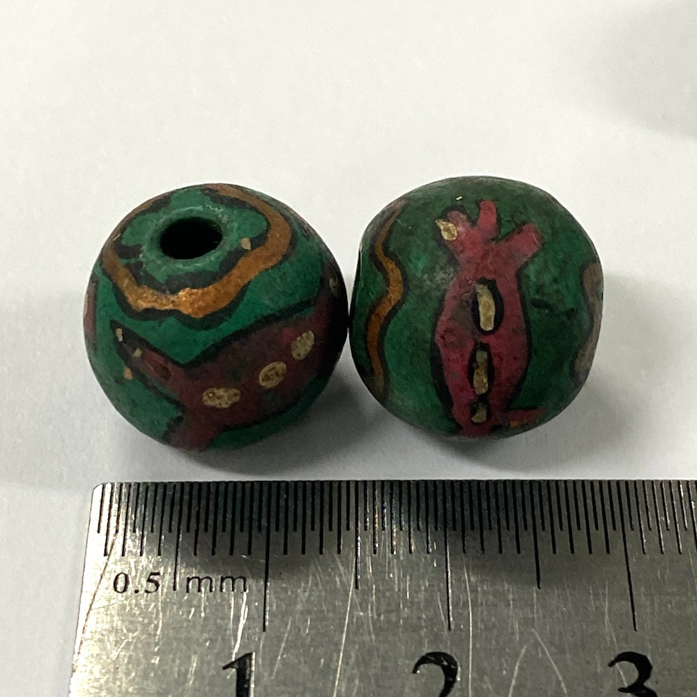 Two green vintage ceramic beads with decorative patterns on a white background, measured against a ruler.