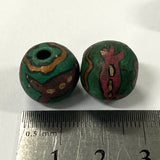 Two green vintage ceramic beads with decorative patterns on a white background, measured against a ruler.