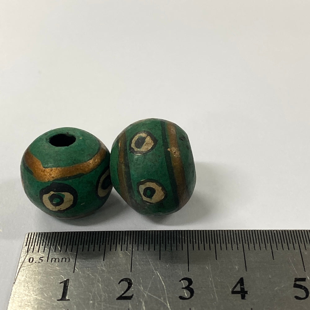 Two green beads with gold accents on a white background, measured against a ruler.