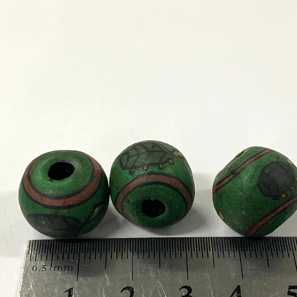 Three green beads with brown and black turtle patterns on a white background, with a ruler for scale.