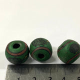 Three green beads with brown and black turtle patterns on a white background, with a ruler for scale.