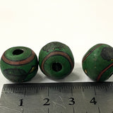 Three green beads with brown accents on a white background, measured against a ruler.