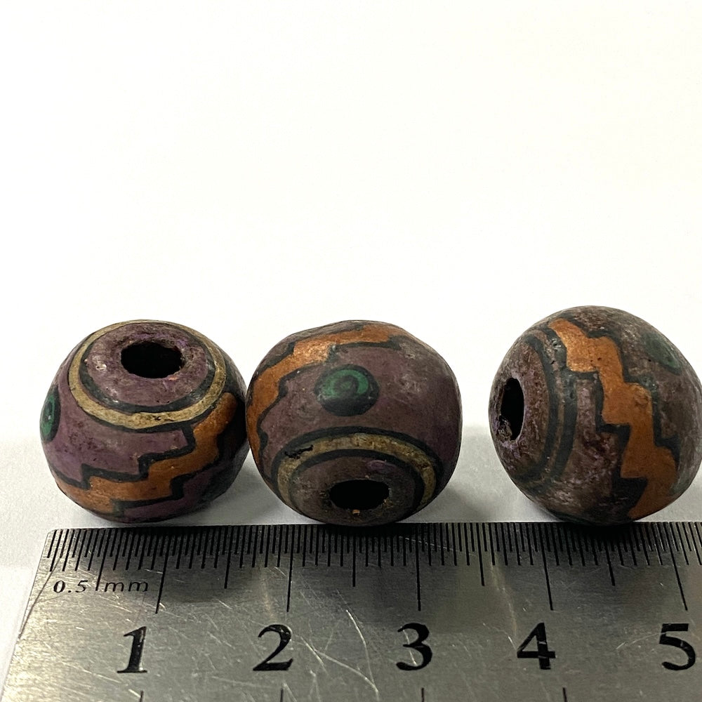 Three purple vintage ceramic beads with a decorative pattern on a ruler for scale.