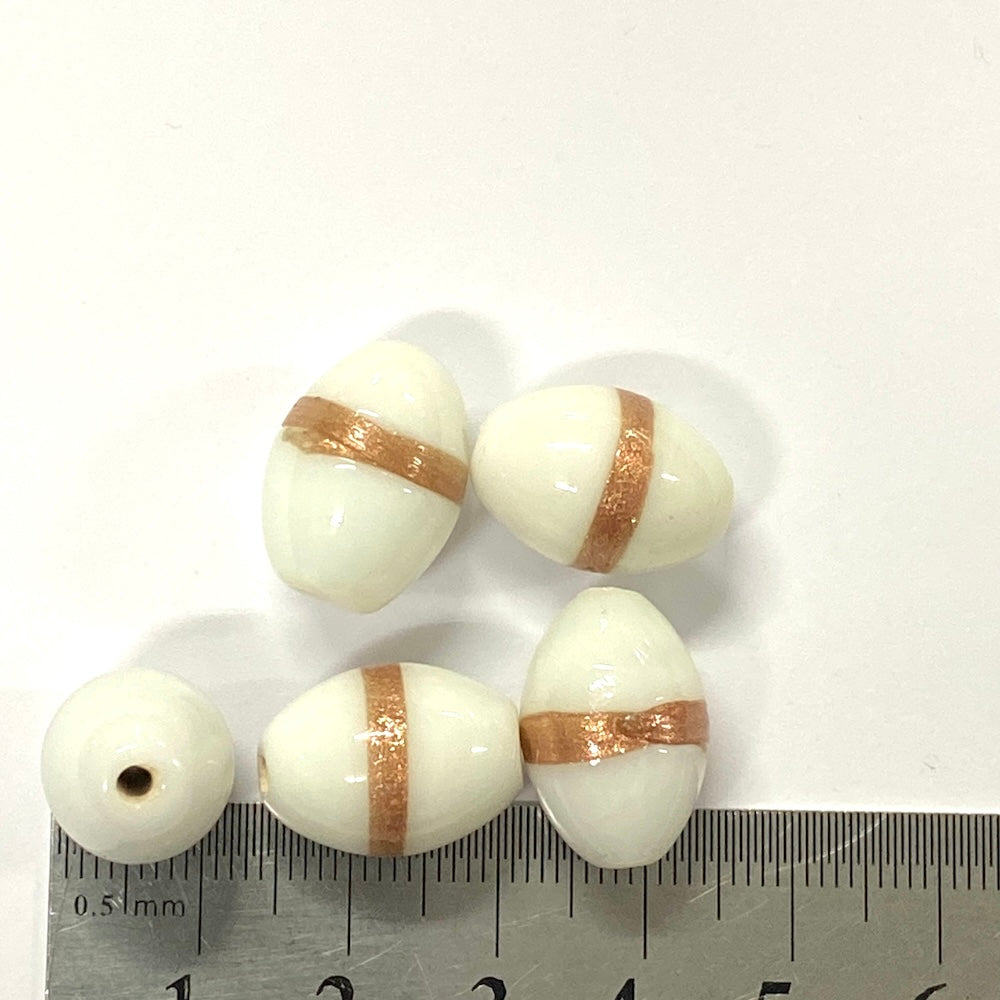 White beads with gold stripes on a white background with a ruler for scale.