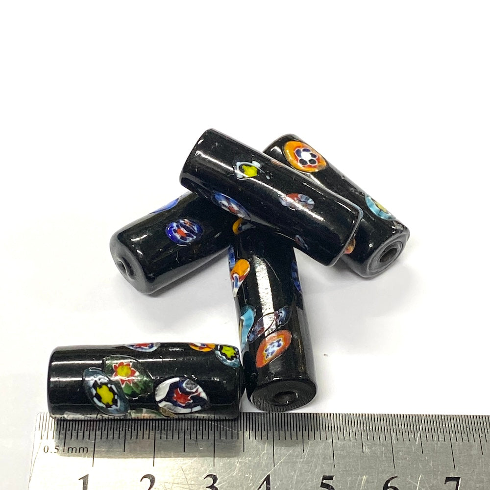 Black cylindrical beads with colorful patterns on a white background, with a ruler for scale.