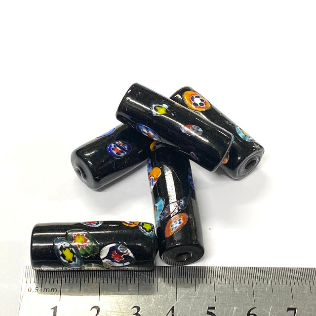 Black cylindrical beads with colorful patterns on a white background, with a ruler for scale.